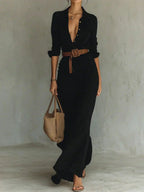 Woman wearing a black lapel collar wrap maxi dress with a brown belt, studio setting