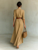 Woman wearing a tan lapel collar belted maxi dress, back view in a studio setting