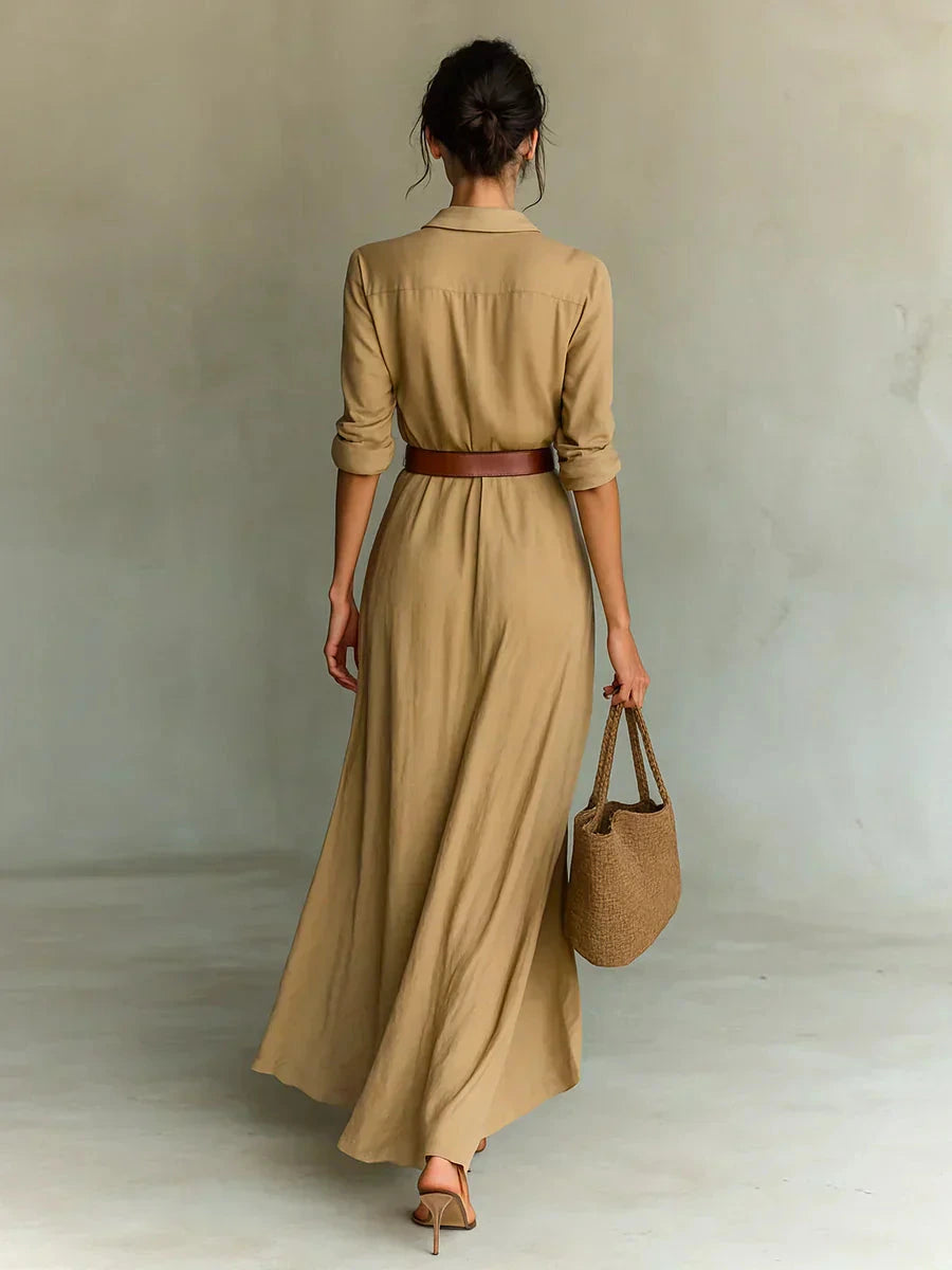 Woman wearing a tan lapel collar belted maxi dress, back view in a studio setting