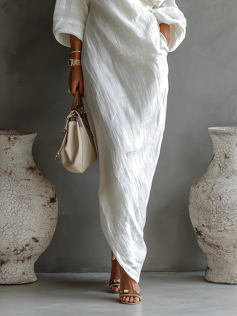 Woman wearing a white one-shoulder draped maxi dress, close-up of the skirt