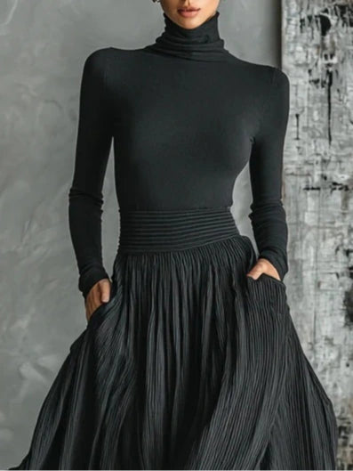 Woman wearing a black pleated maxi skirt with a black turtleneck top, close-up front view