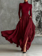 Woman wearing a dark red pleated maxi skirt with a dark red turtleneck top, studio setting