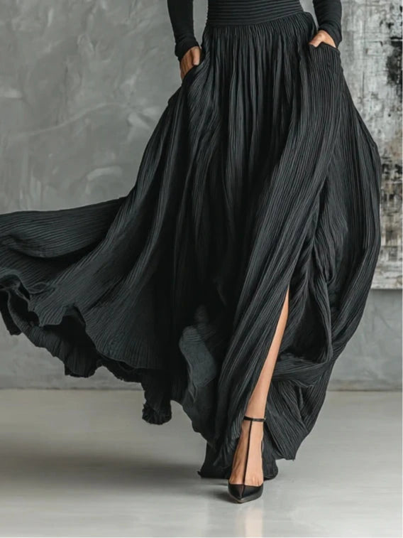 Close-up of a black pleated maxi skirt showing the pleat and slit detail