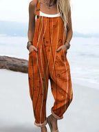 Woman wearing a rust-orange sleeveless jumpsuit with a white line print standing on a sandy beach