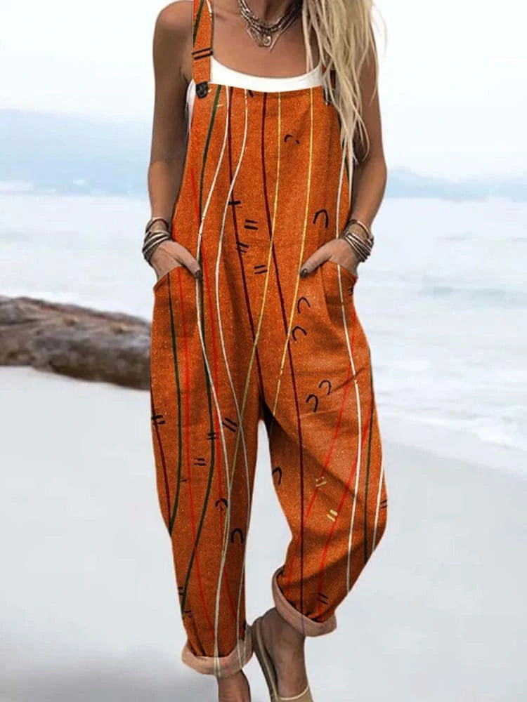 Woman wearing a rust-orange sleeveless jumpsuit with a white line print standing on a sandy beach
