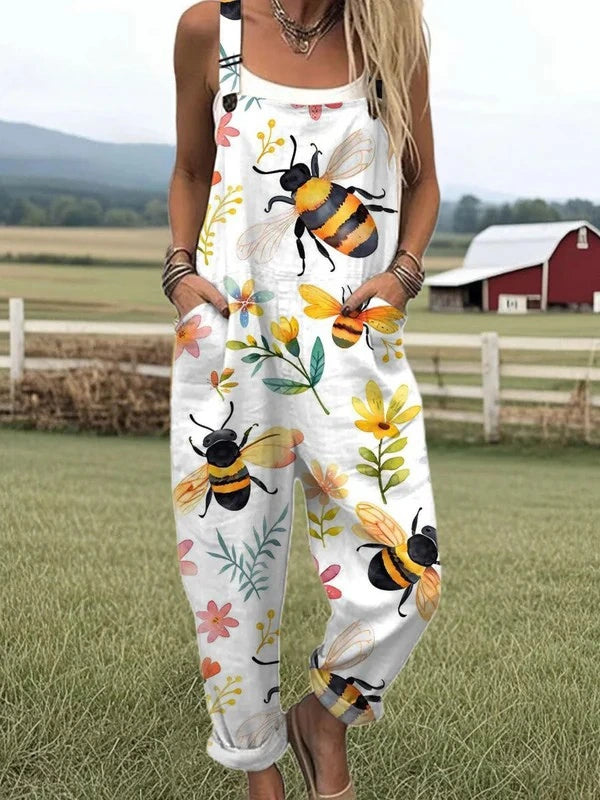 Woman wearing a white jumpsuit with a bee and floral blossom print standing in a farm field near a red barn