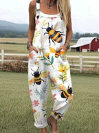 Woman wearing a white jumpsuit with a bee and floral blossom print standing in a farm field near a red barn