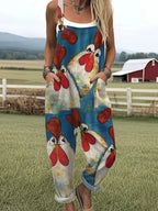 Woman wearing a teal chicken print sleeveless button-front overall jumpsuit standing in a farm field near a red barn