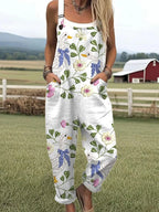 Woman wearing a white purple and blue floral print sleeveless wide-leg overall jumpsuit standing in a grassy field near a red barn