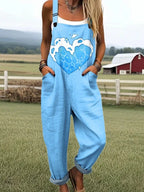 Woman wearing a light-blue heart print sleeveless overall jumpsuit standing in a farm field near a red barn
