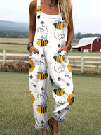 Woman wearing a white honeybee print sleeveless button-down overall jumpsuit standing in a farm field near a red barn