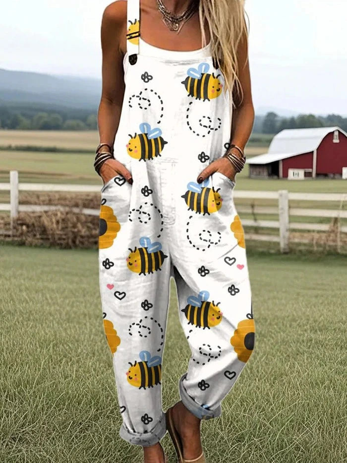 Woman wearing a white honeybee print sleeveless button-down overall jumpsuit standing in a farm field near a red barn