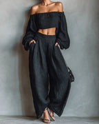 Woman wearing a black off-shoulder wide-leg jumpsuit in a studio setting