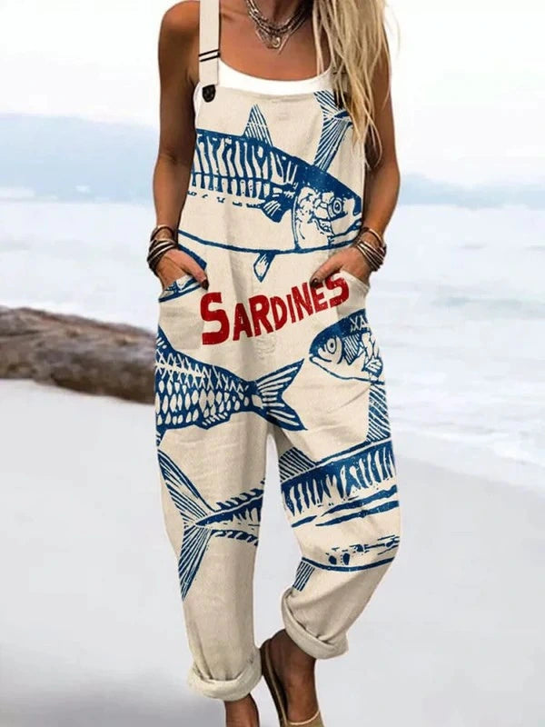 Woman wearing a cream jumpsuit with a blue sardine fish print standing on a sandy beach