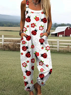 Woman wearing a white jumpsuit with a red ladybug and floral print standing in a farm field near a red barn
