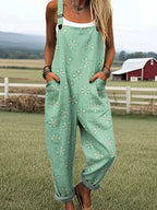 Woman wearing a mint-green daisy print sleeveless wide-leg overall jumpsuit standing in a grassy farm field