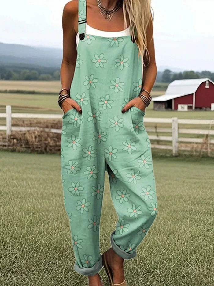 Woman wearing a mint-green daisy print sleeveless wide-leg overall jumpsuit standing in a grassy farm field