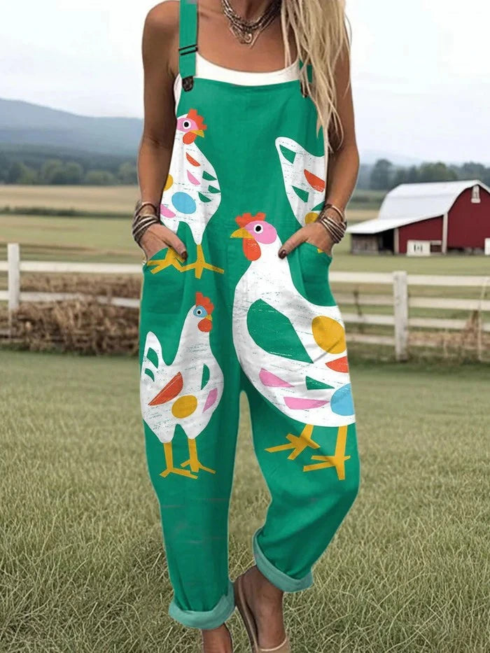 Woman wearing a teal-green jumpsuit with a white rooster and hen print standing in a farm field near a red barn