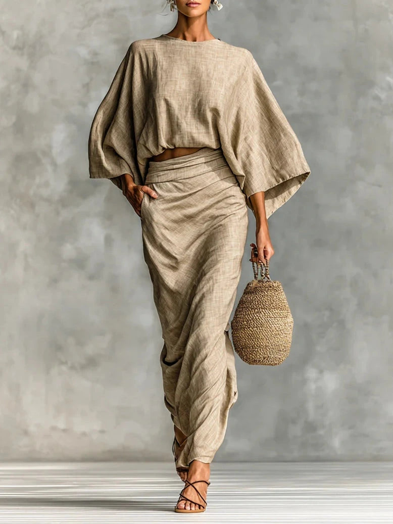Woman wearing a khaki two-piece coordinating outfit with an oversized top and wide-leg wrap skirt, holding a straw bag