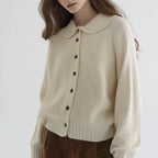 Woman wearing a cream button-up collared sweater, front view in a studio setting