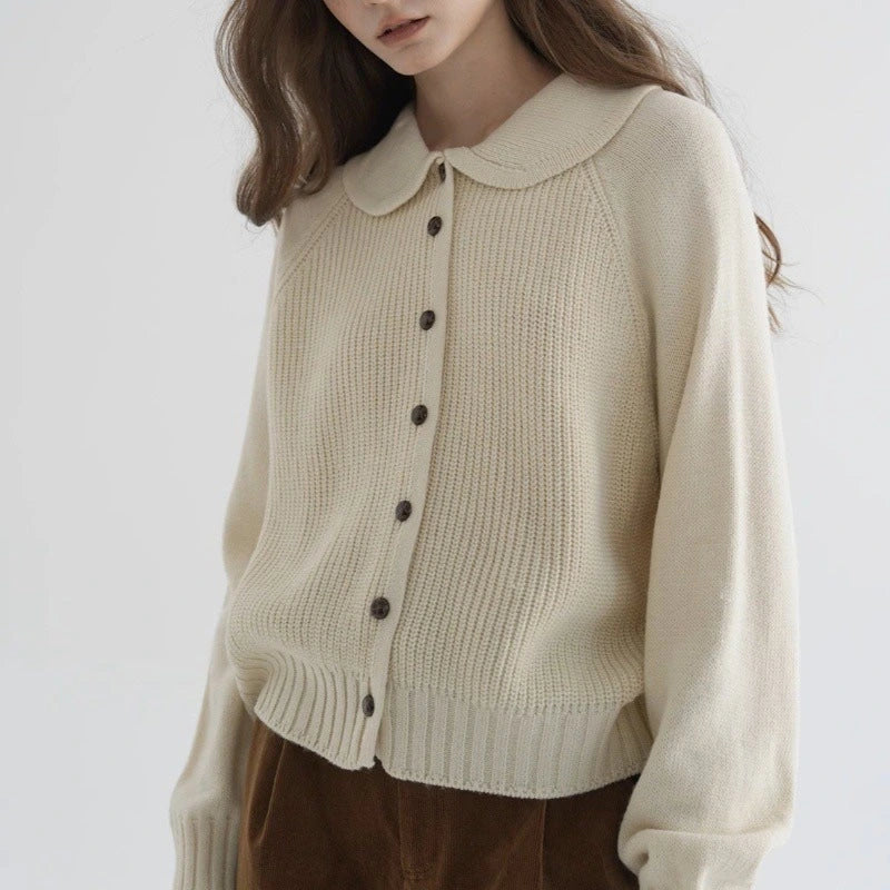 Woman wearing a cream button-up collared sweater, front view in a studio setting