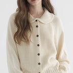 Woman wearing a cream button-up collared sweater, alternate pose in a studio setting