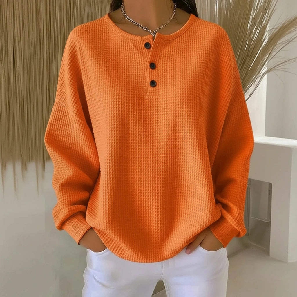 Woman wearing an orange long sleeve waffle knit sweater in a studio setting