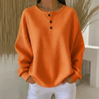 Woman wearing an orange long sleeve waffle knit sweater in a studio setting