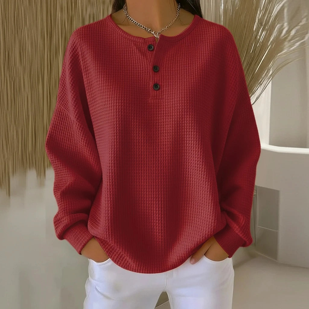 Woman wearing a red long sleeve waffle knit sweater in a studio setting
