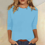 Woman wearing a light blue crew neck three-quarter sleeve top in a studio setting