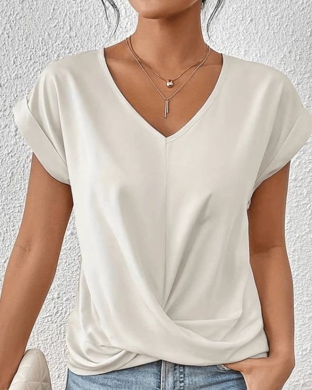 Woman wearing a white v-neck twist front short sleeve top in a studio setting