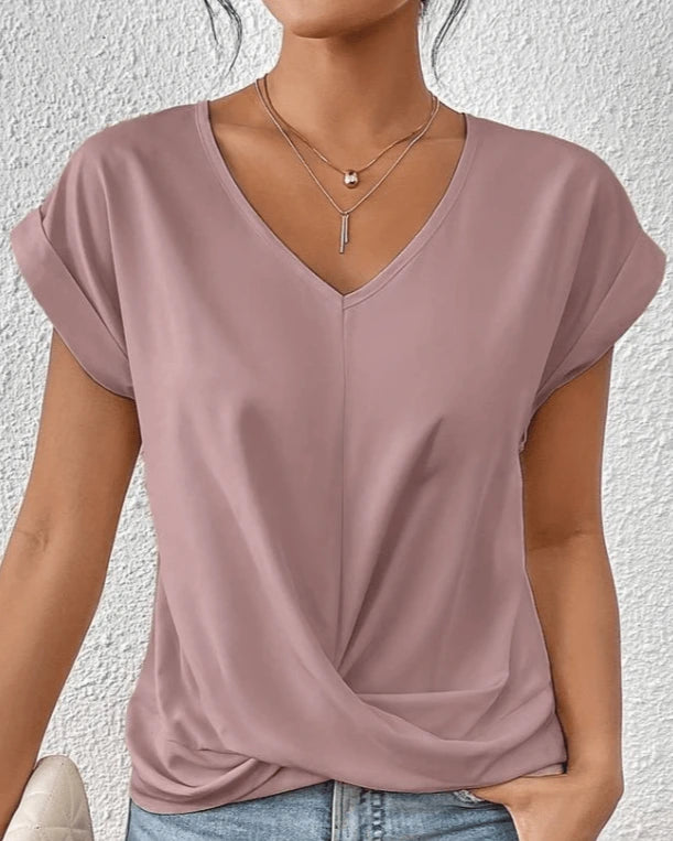 Woman wearing a pink v-neck twist front short sleeve top in a studio setting