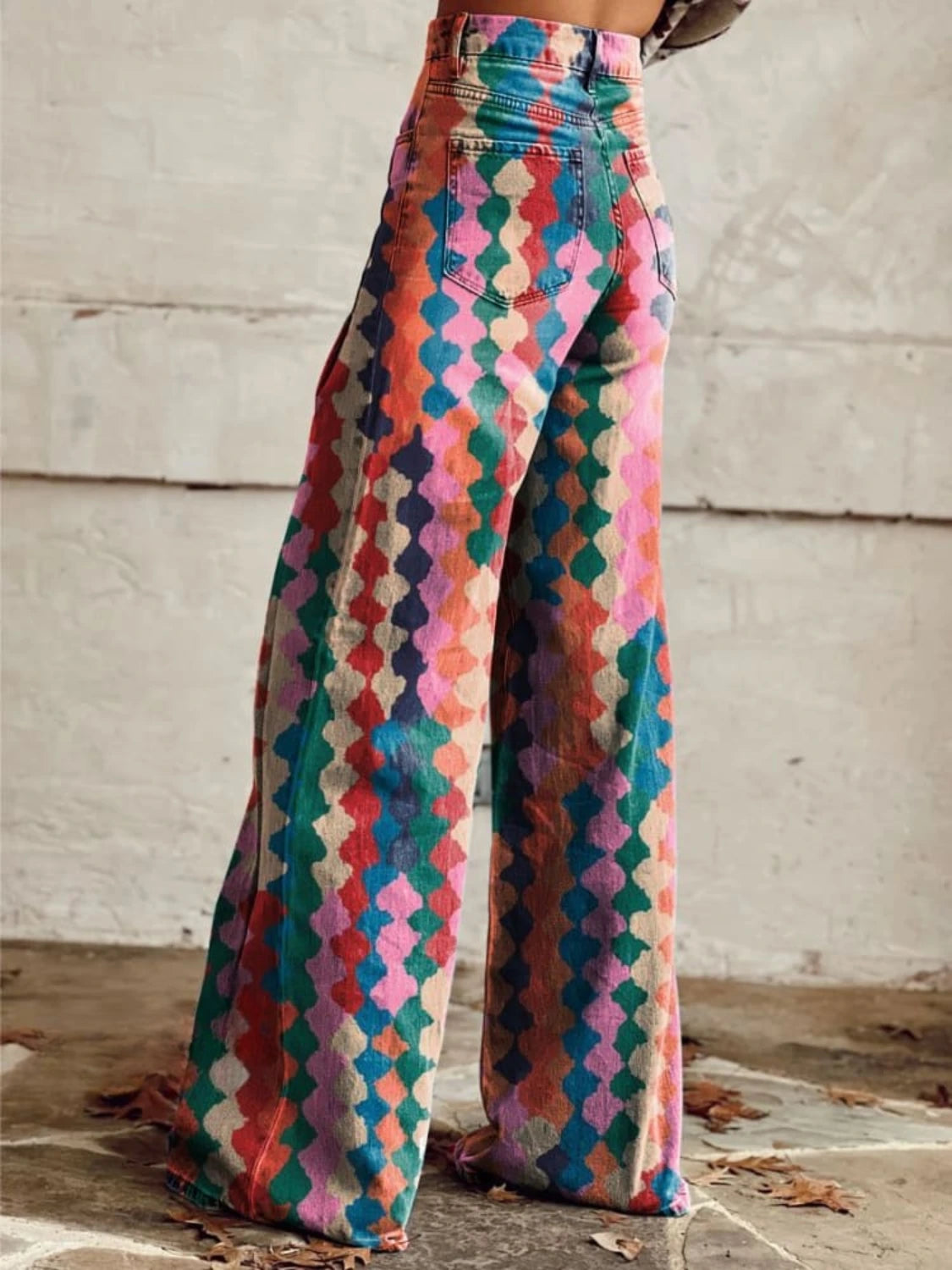 Woman wearing multicolor bohemian chic high-waisted wide-leg trousers with a geometric diamond print, back view