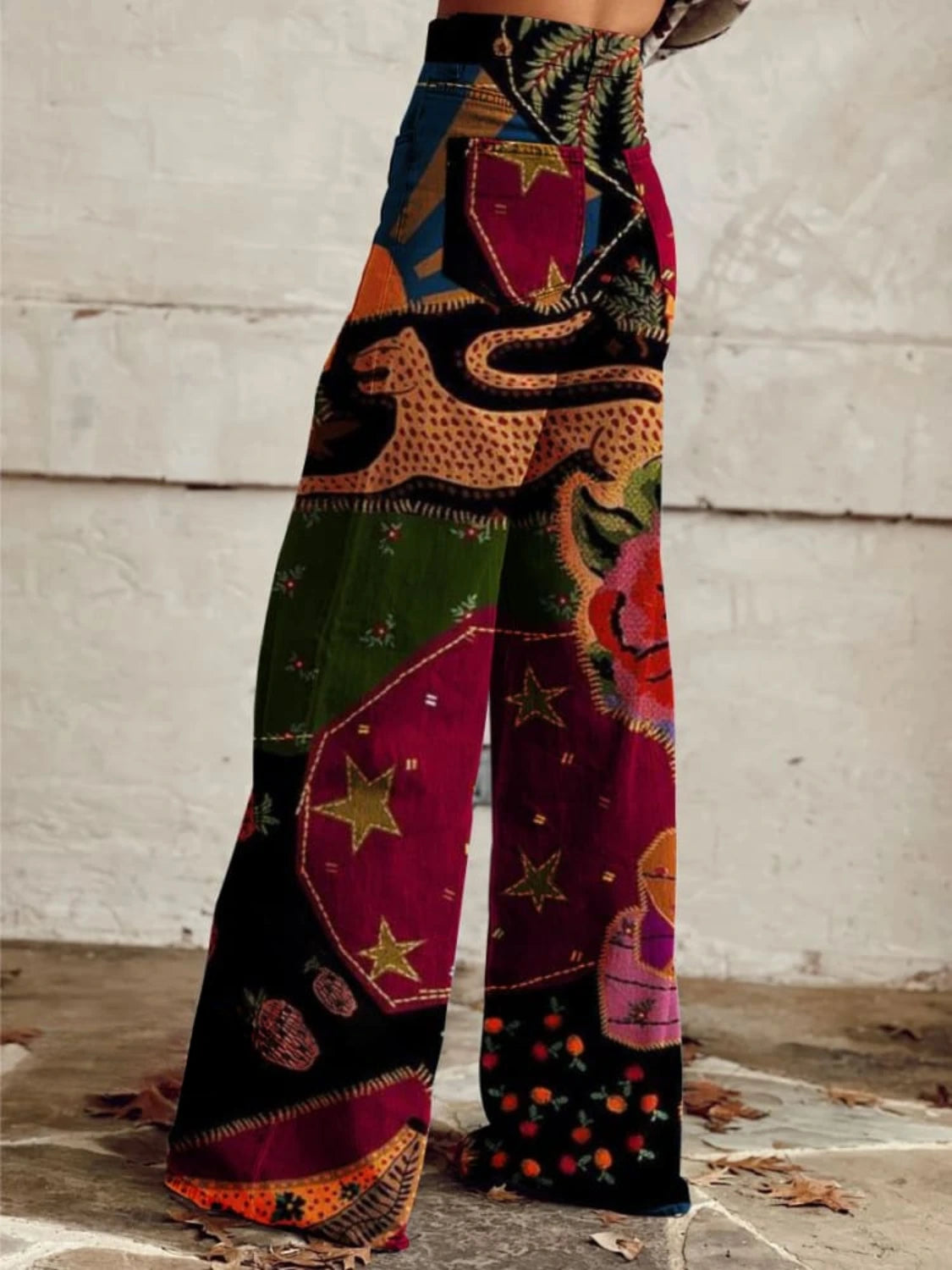 Woman wearing red and black bohemian print wide-leg trousers with gold star and floral details, side view